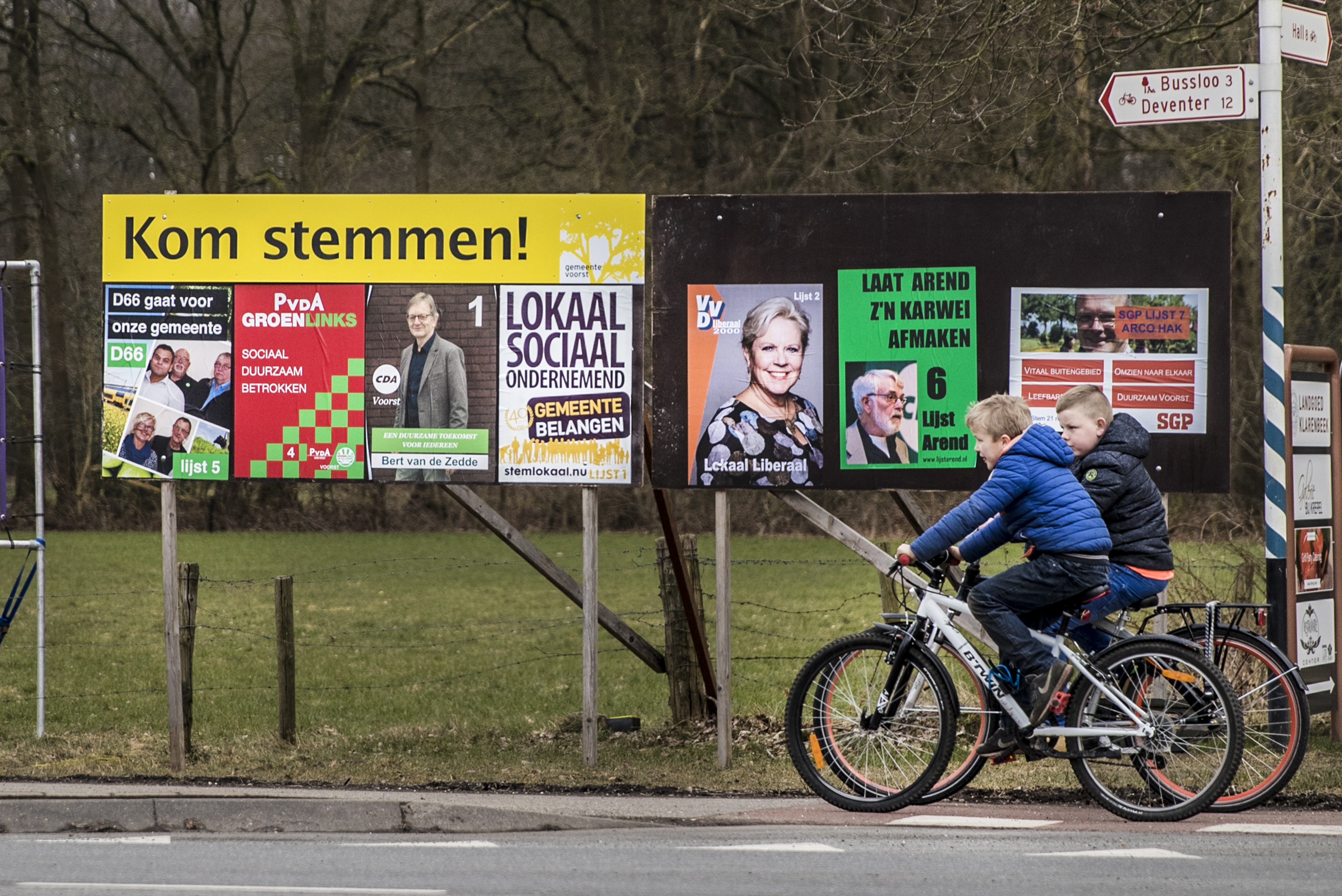 Kinderen fietsen langs een verkiezingsbord in Klarenbeek.