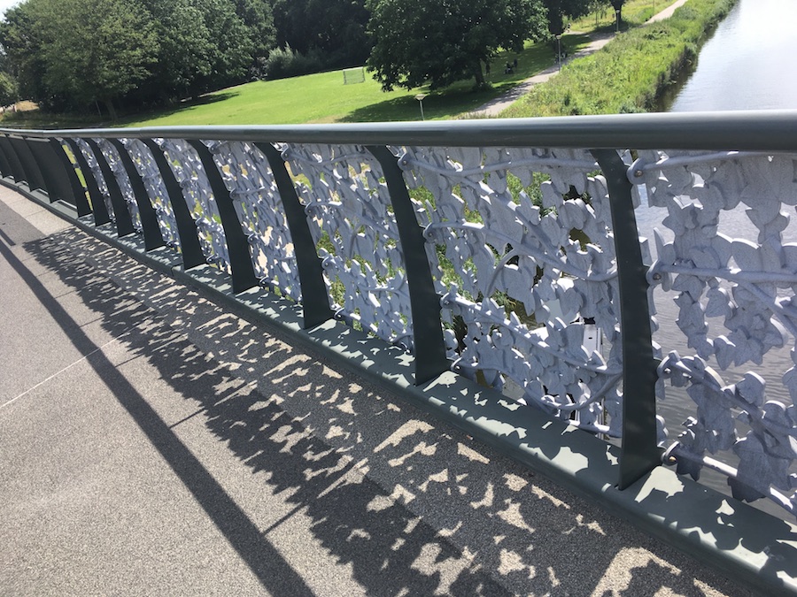 Fietsbrug in het Noorderpark met gietijzeren bladeren die een bladerachtige schaduw geven.