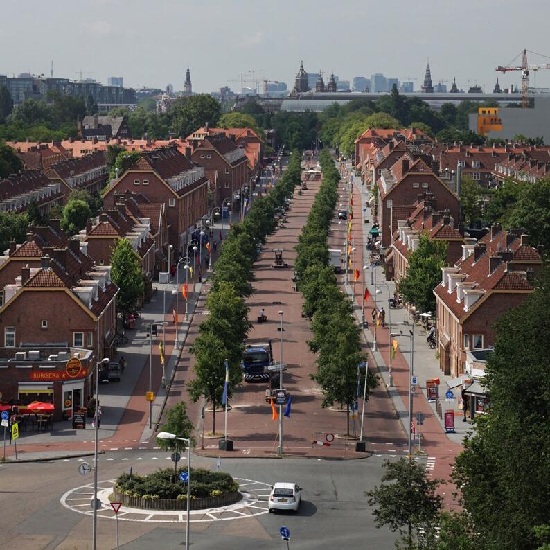 Luchtfoto van een straat met oranje vlaggen langs de fietspaden. Op de voorgrond een groene rotonde.