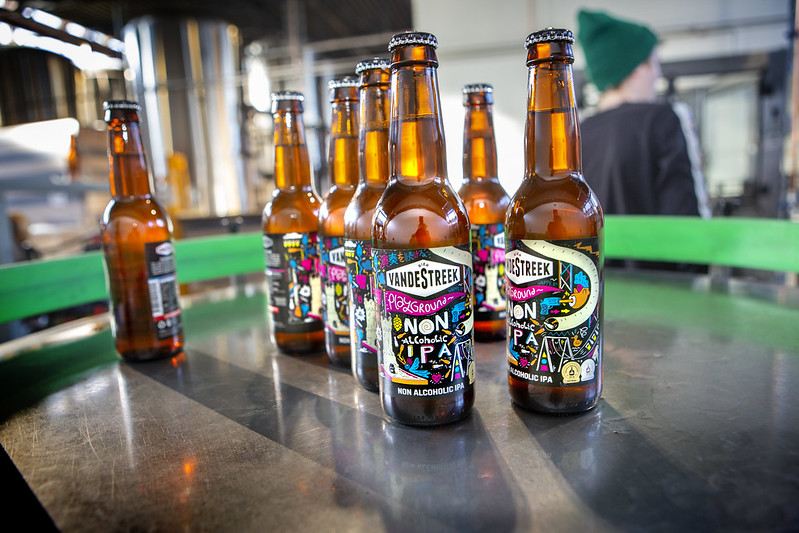 Stuk of tien bierflesjes met kleurige etiketten waarop staat 'vandestreek' en 'non-alcoholic IPA'.