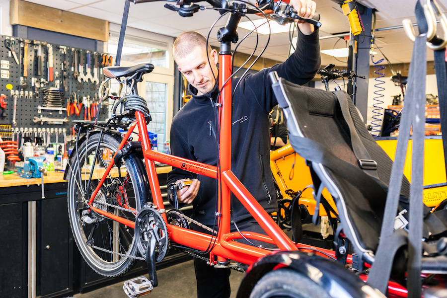 Repareren van een oranje aangepaste fiets die in de beugels hangt.