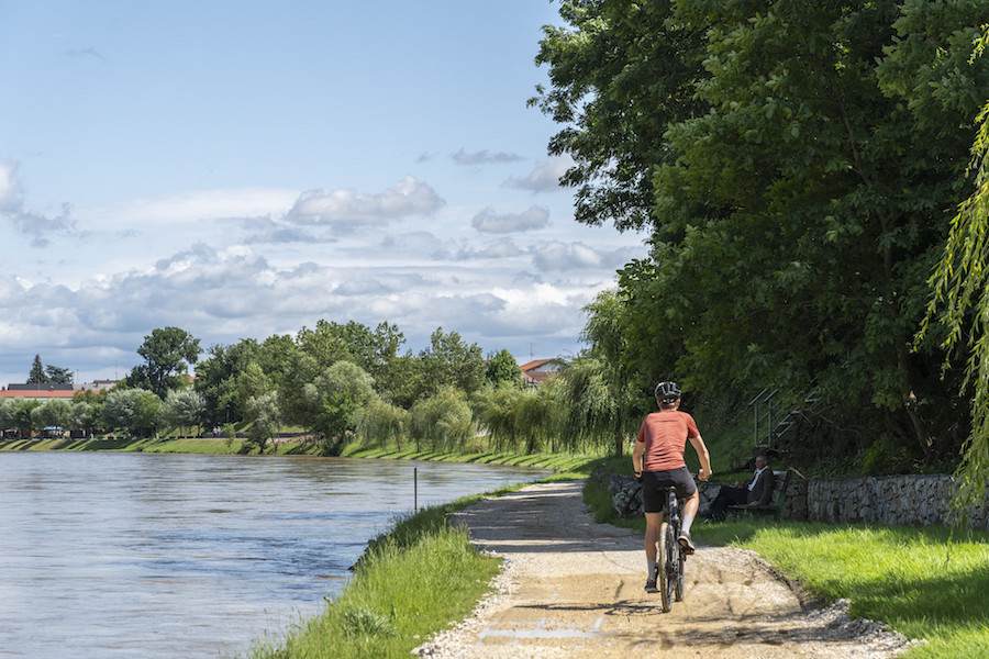 Fietser op de rug over een zandpad langs een groene rivieroever.