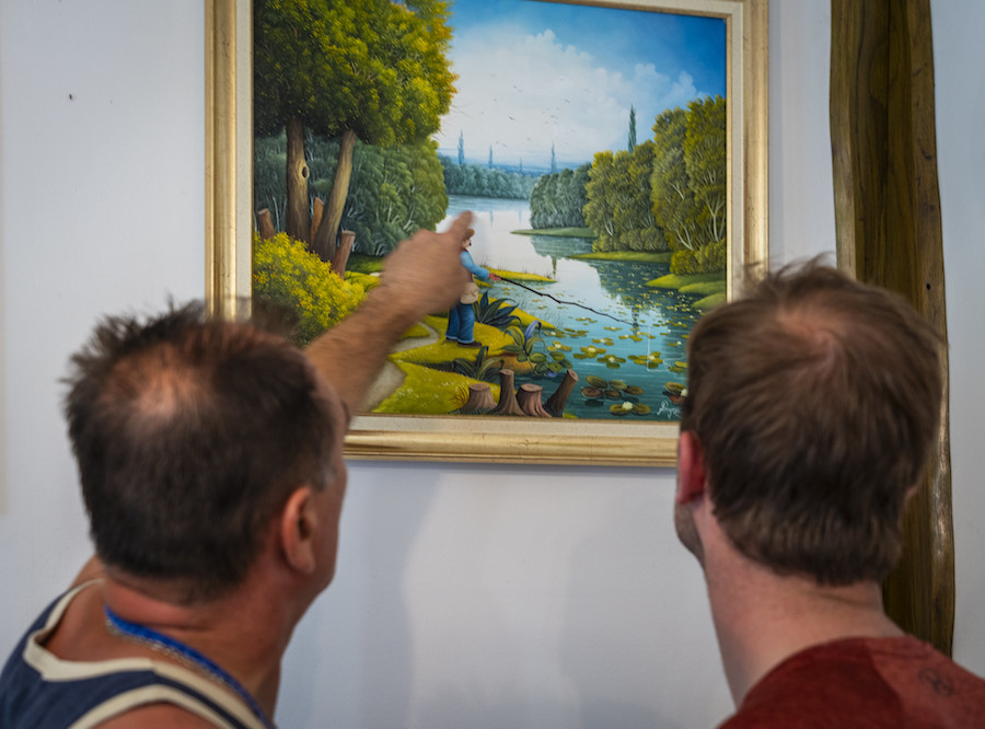 man wijst man naast hem op een detail in een schilderij van een rivier