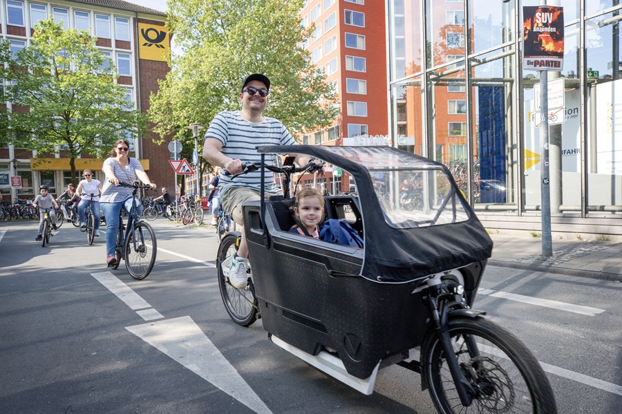 Jonge man in streepshirt fiets op bakfiets met kind erin.