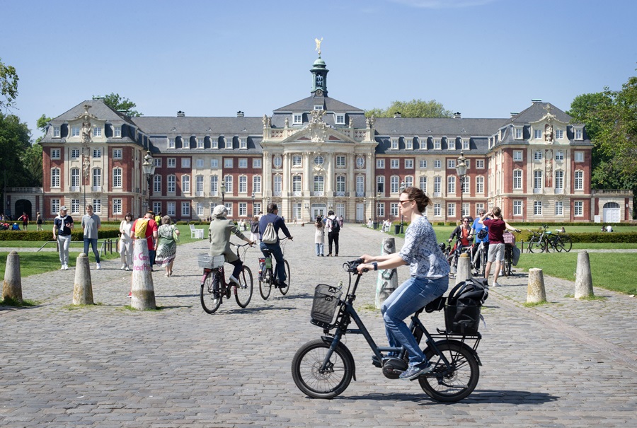 Vrouw met zonnebril fiets langs kasteel over de Groene Promenade rond Münster.