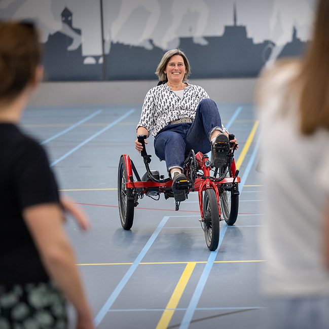 Fietser probeert een rode driewielfiets uit.