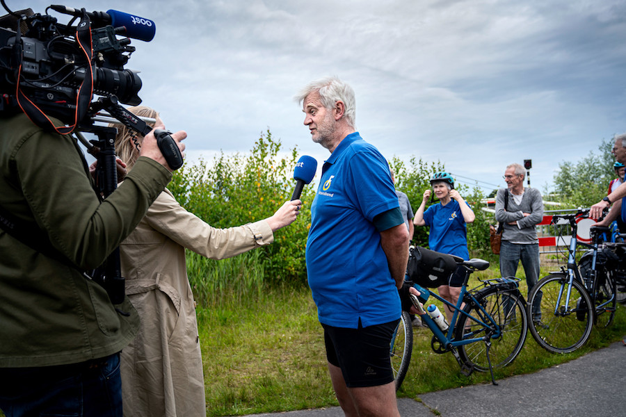 Man in blauw shirt met Fietsersbondlogo staat cameraploeg te woord in groene omgeving bij afgesloten brug in Giethoorn.