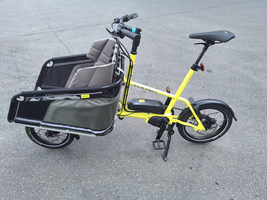 Gele bakfiets met sportief zadel en stoffen zitjes in bak voor.