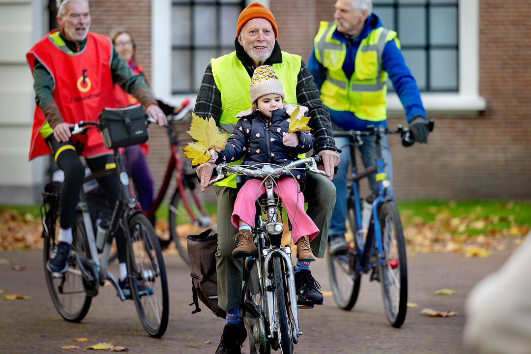 Vrijwilligers van de Fietsersbond fietsen een rondje voor het provinciehuis in Haarlem. Ze dragen een geel of rood gekleurd hesje met het logo van de Fietsersbond erop.