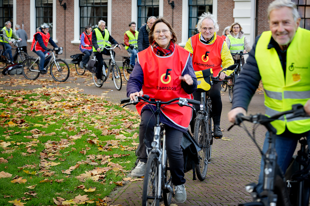 Vrijwilligers van de Fietsersbond fietsen een rondje voor het provinciehuis in Haarlem. Ze dragen een geel of rood gekleurd hesje met het logo van de Fietsersbond erop.