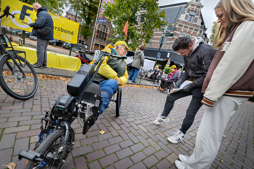Een man zet een handtekening onder de petitie fietsparkeren van de Fietsersbond. Naast hem zit een vrijwilliger van de Fietsersbond in een driewielfiets.