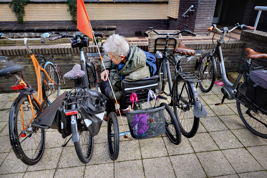Fietser met driewielfiets parkeert haar fiets tussen andere geparkeerde fietsen. Er is weinig ruimte om de fiets op slot te zetten en af te stappen.