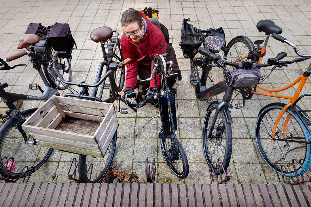 Fietser met driewielfiets parkeert haar fiets tussen andere geparkeerde fietsen. Er is weinig ruimte om de fiets op slot te zetten en af te stappen.