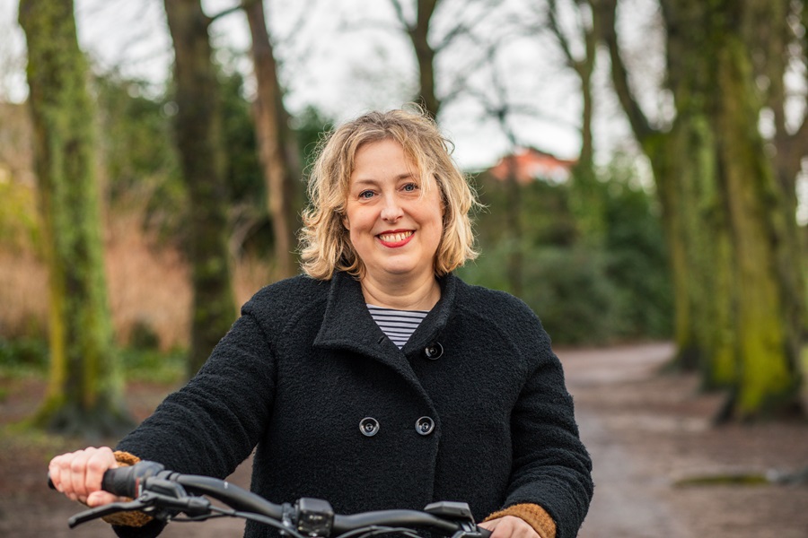 Lachende vrouw met rode lippenstift in een bomenlaan met haar handen aan het stuur.