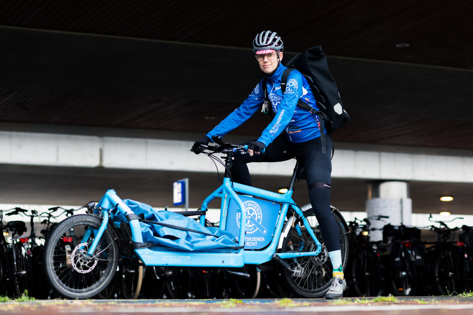 Foto van Fietskoerier in sportieve blauwe kleding op sportieve blauwe bakfiets.