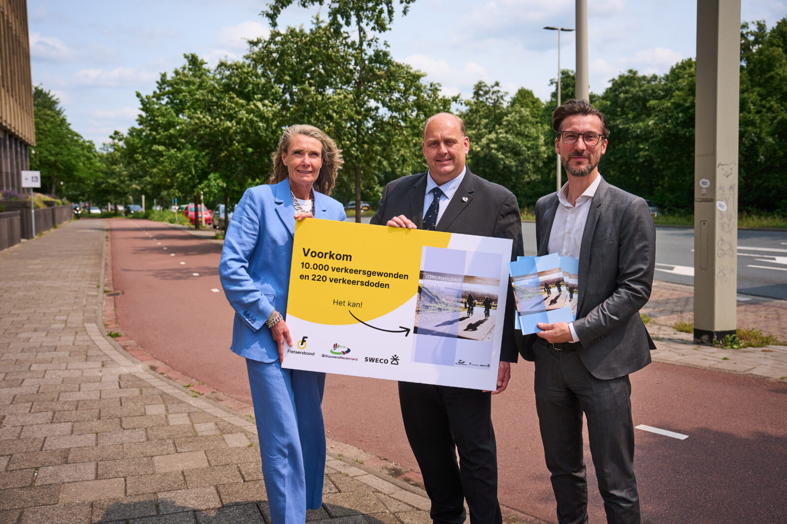 Esther van Garderen en Bouwend Nederland overhandigen het rapport over veiligheid fietsroutes in Nederland aan Frederik Zevenbergen (VVD), gedeputeerde Provincie Zuid-Holland. Op de achtergrond een fietspad.