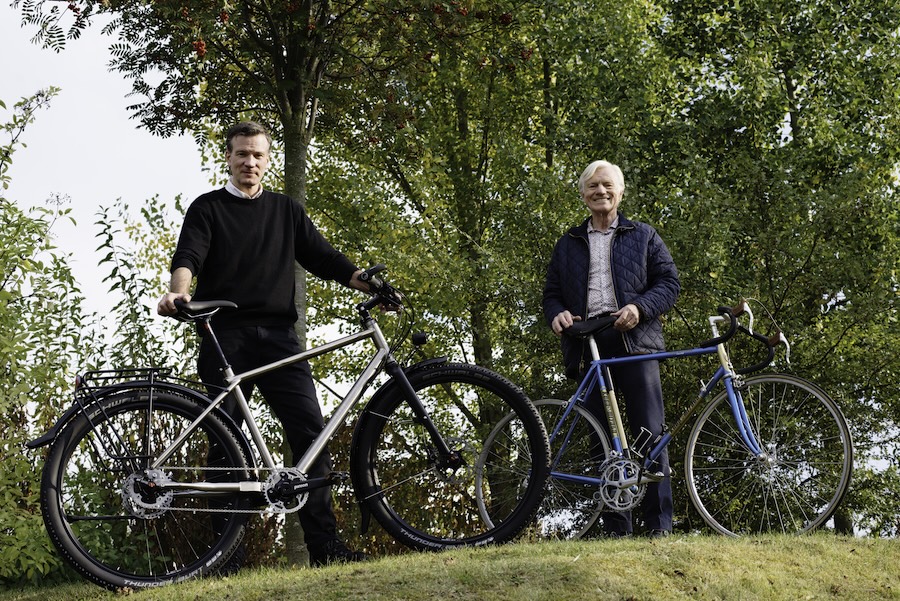 Op een heuveltje staan twee mannen met een fiets.