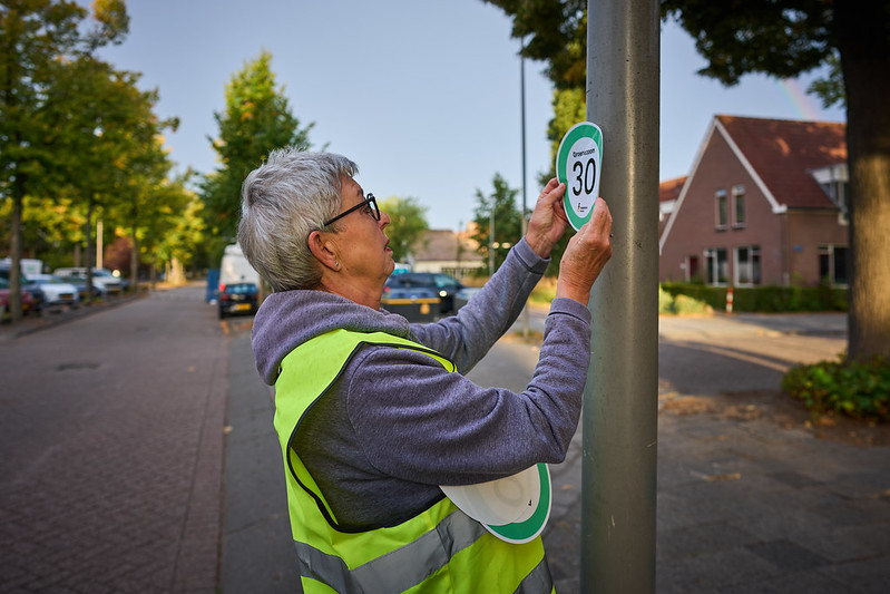 Vrijwilliger van de Fietsersbond plakt 30 km/u sticker op lantaanpaal
