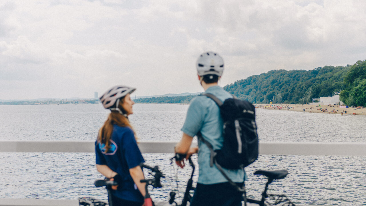 Een man en een vrouw met fietsen en een helm op kijken over water uit.