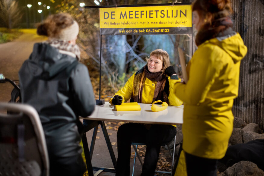 In 2022 organiseerde de Fietsersbond de Meefietslijn. Tijdens speciale Meefietslijnavonden is het voor fietsers mogelijk om telefonisch te worden vergezeld. Een fietser praat met de twee dames van de Meefietslijn (in gele jas en met geel bord met De Meefietslijn). Op tafel staat een ouderwetse telefoon.