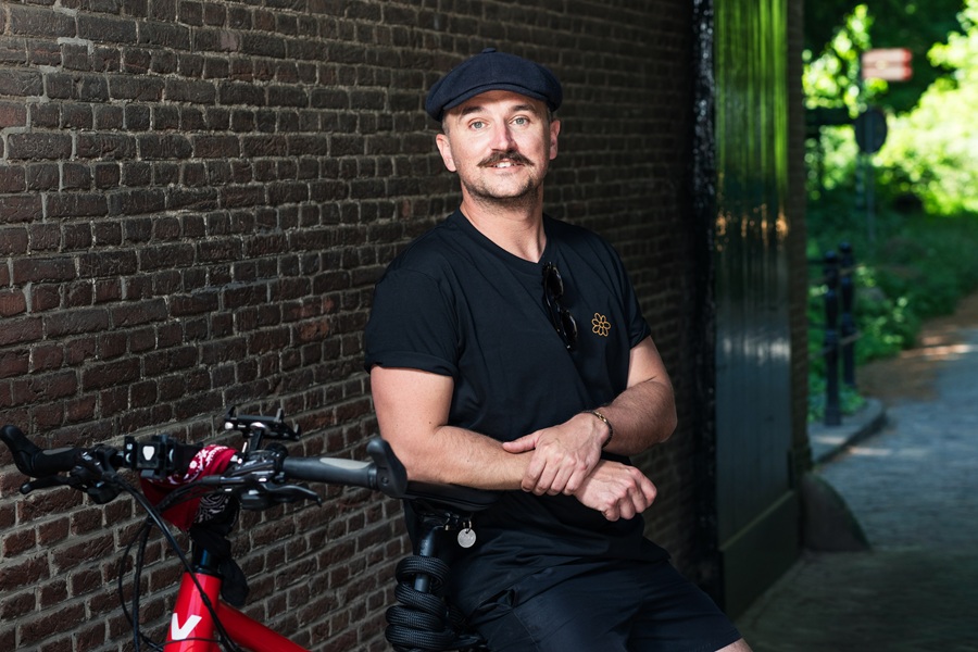 Man met pet leunt op het stuur van een rode fiets