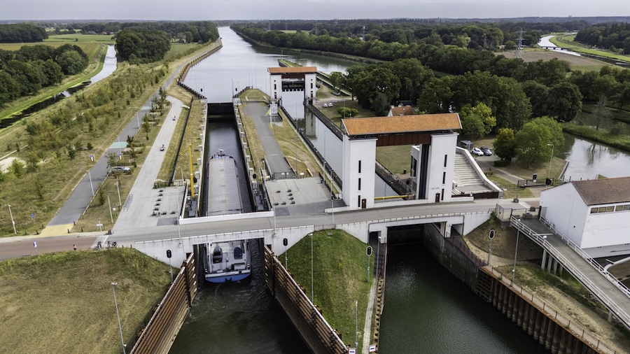 Dronefoto van een witte sluis met rood dakje in een groene omgeving.