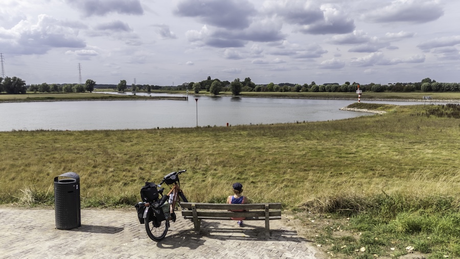 Vrouw op bankje met een bepakte fiets naast zich en uitzicht op de IJssel.