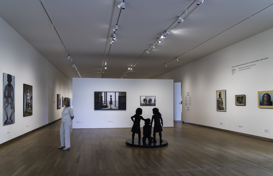 Zaal met kunstwerken aan de muur en een beeldhouwwerk van kinderen.