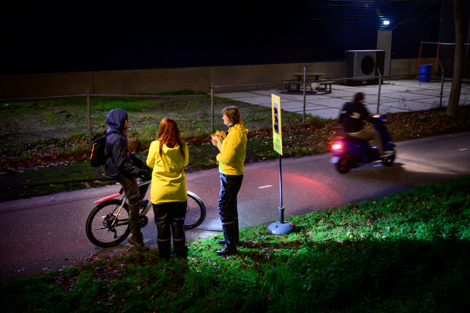 Twee vrouwen met gele jassen praten met een mountainbiker op een donker fietspad.