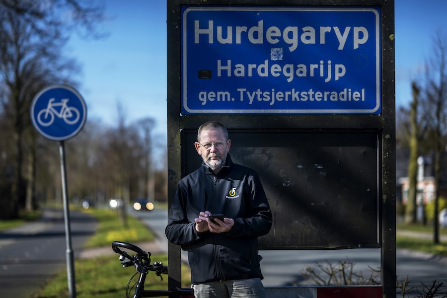 Kees van Stijn draagt ene Fietsersbondjas en staat bij een bord waarop staat 'Hurdegaryp Hardegarijp Gem. Tystsjerkstreradiel