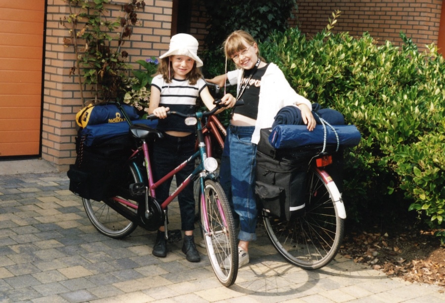 Twee meisje met volgepakte fiesten voor ene heg bij een garage.