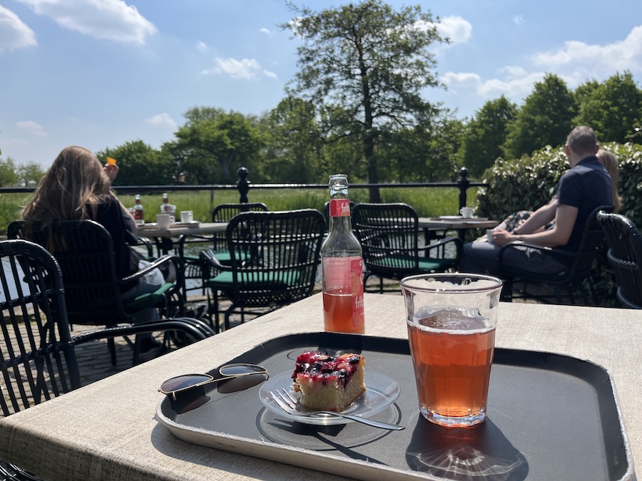 Flesje met rood sap en een taartje met op achtergrond een riviertje en bomen.
