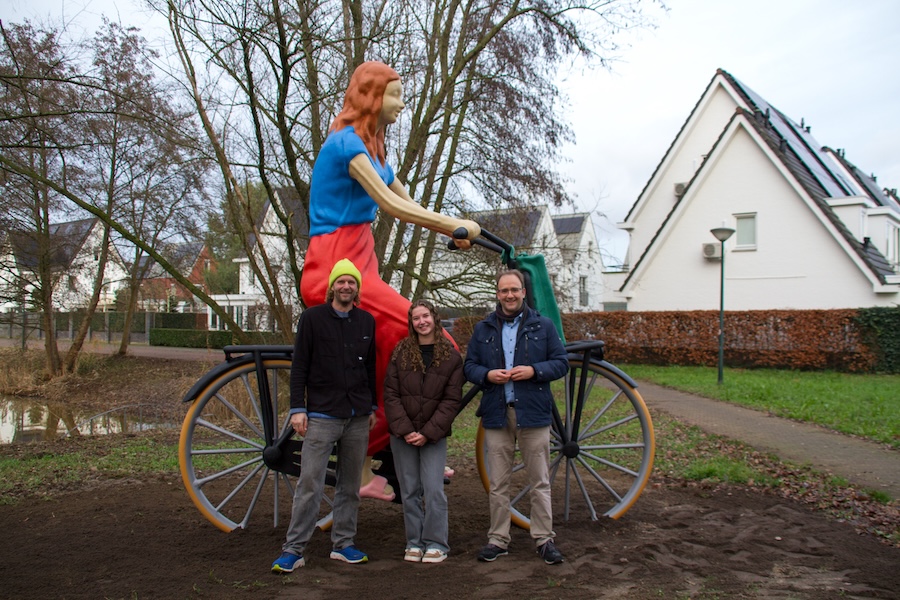 Twee mannen en de scholiere Kay, die poseerde voor het grote beeld van een scholiere, dat op de achtergrond te zien is.