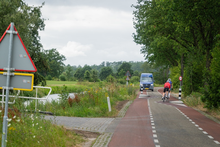 Racefietsers naderen op smal stuk van de weg een bestelbus.