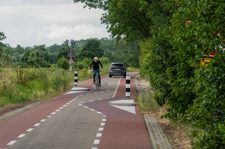 Fietser rijdt over hoekige markeringen tussen twee paaltjes door op smalle weg.