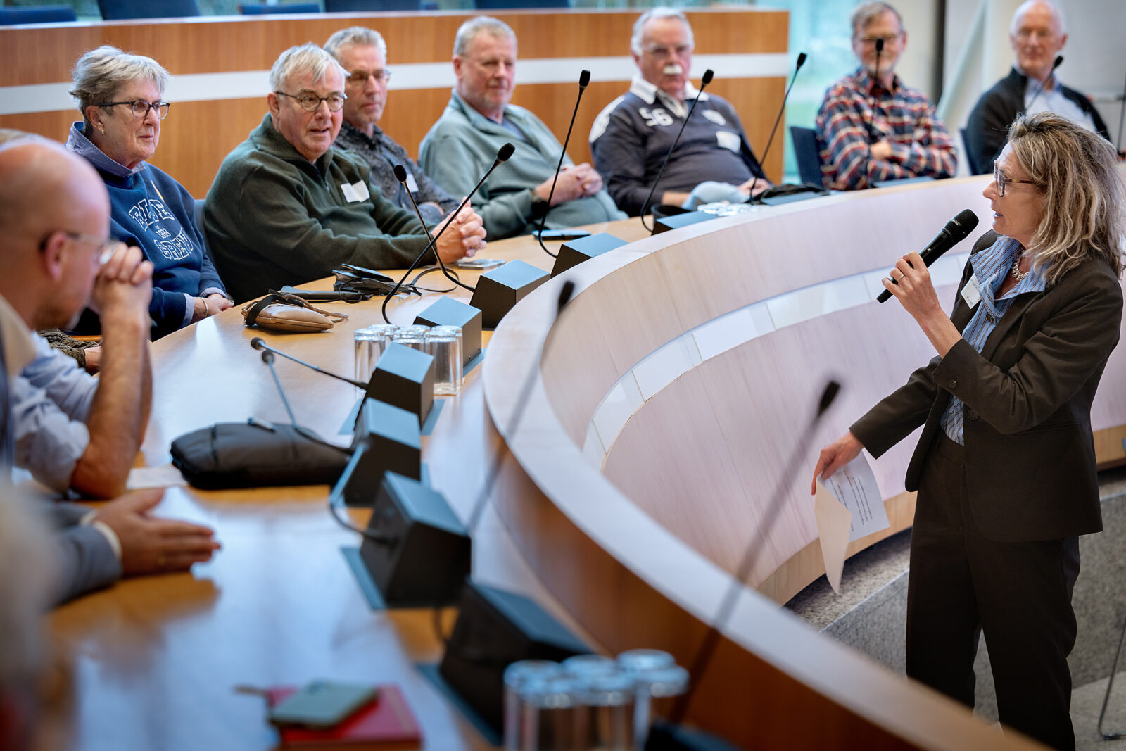 Debatleider Esther van Garderen staat met microfoon in de hand en praat met fietsers die zitten in de Statenzaal achter een spreekmicrofoon.