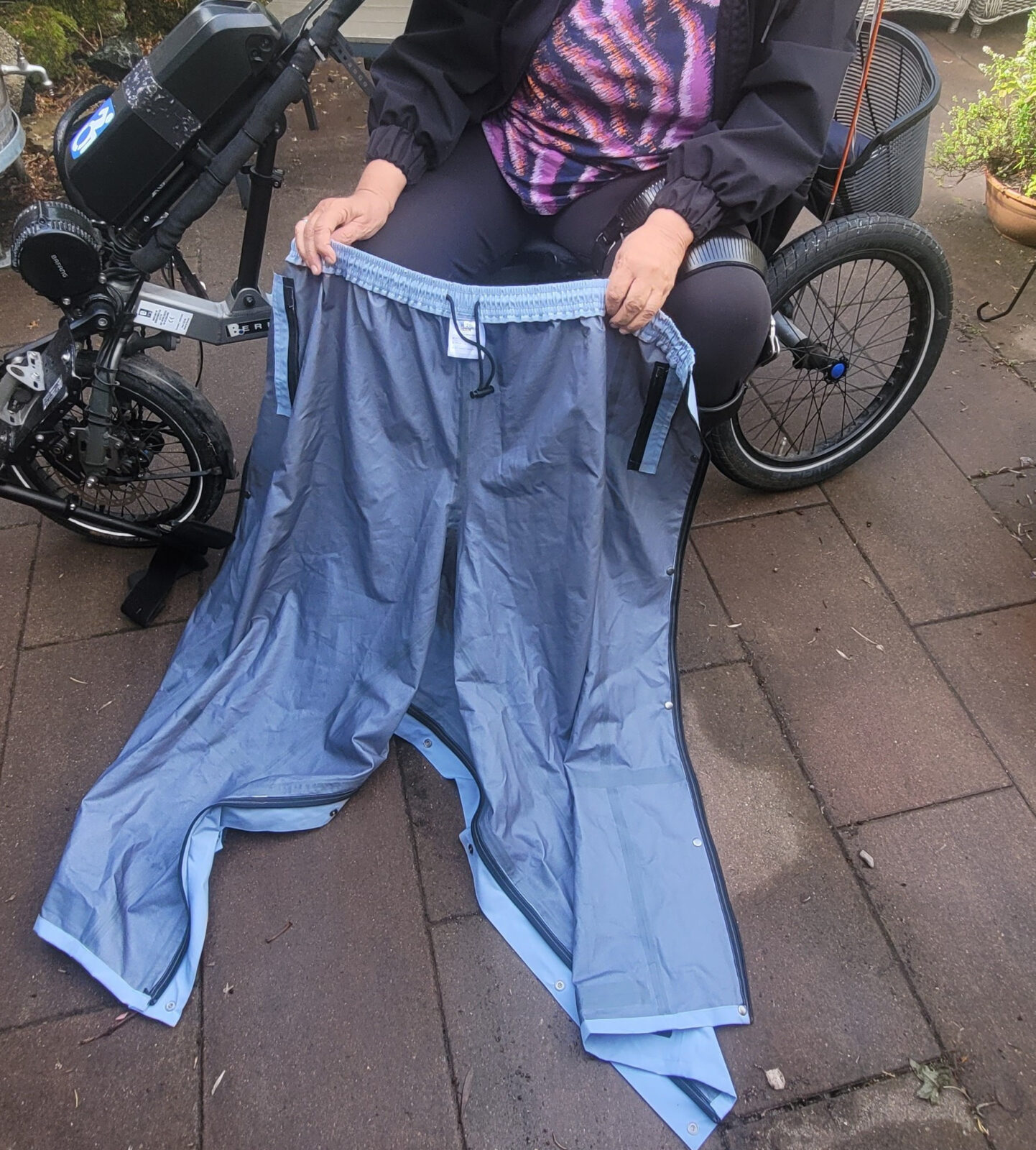 Vrouw demonstreert regenbroek door hem omhoog te houden. 